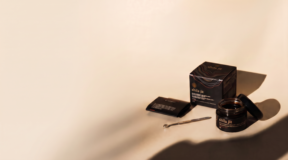 Tarro de resina Shilajit dorado junto a su caja y cuchara dosificadora, sobre fondo crema con una sombra alargada.