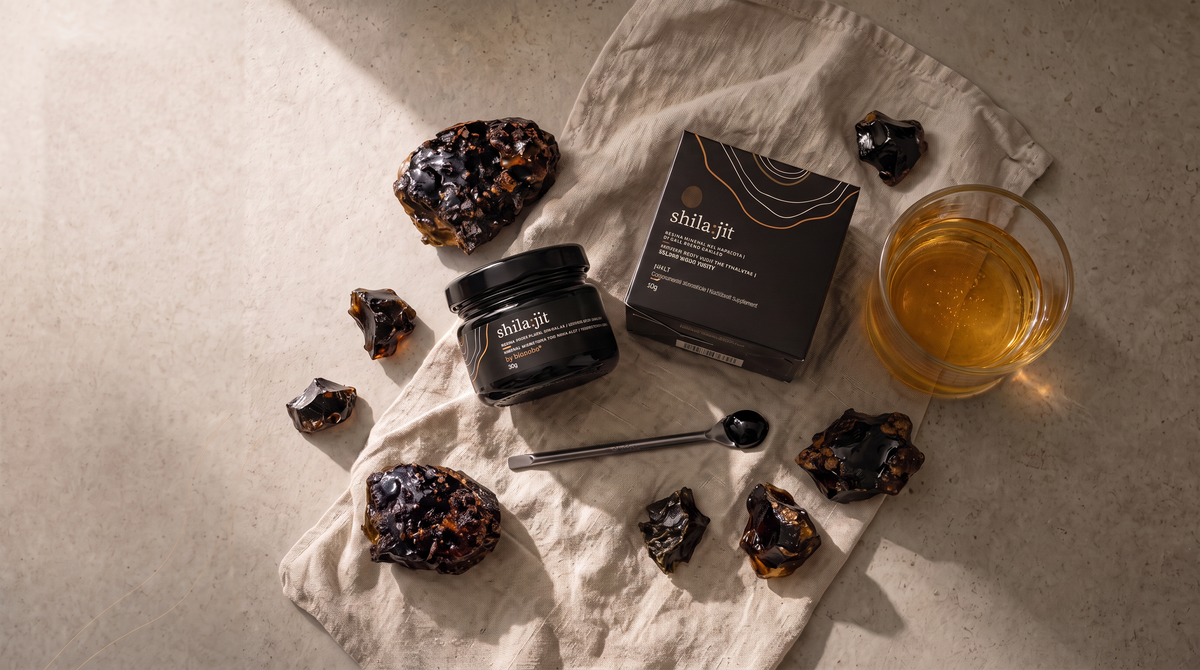Abra el frasco de resina Shilajit de grado dorado Bionobo con su caja, rocas minerales, cuchara medidora y un vaso de agua.