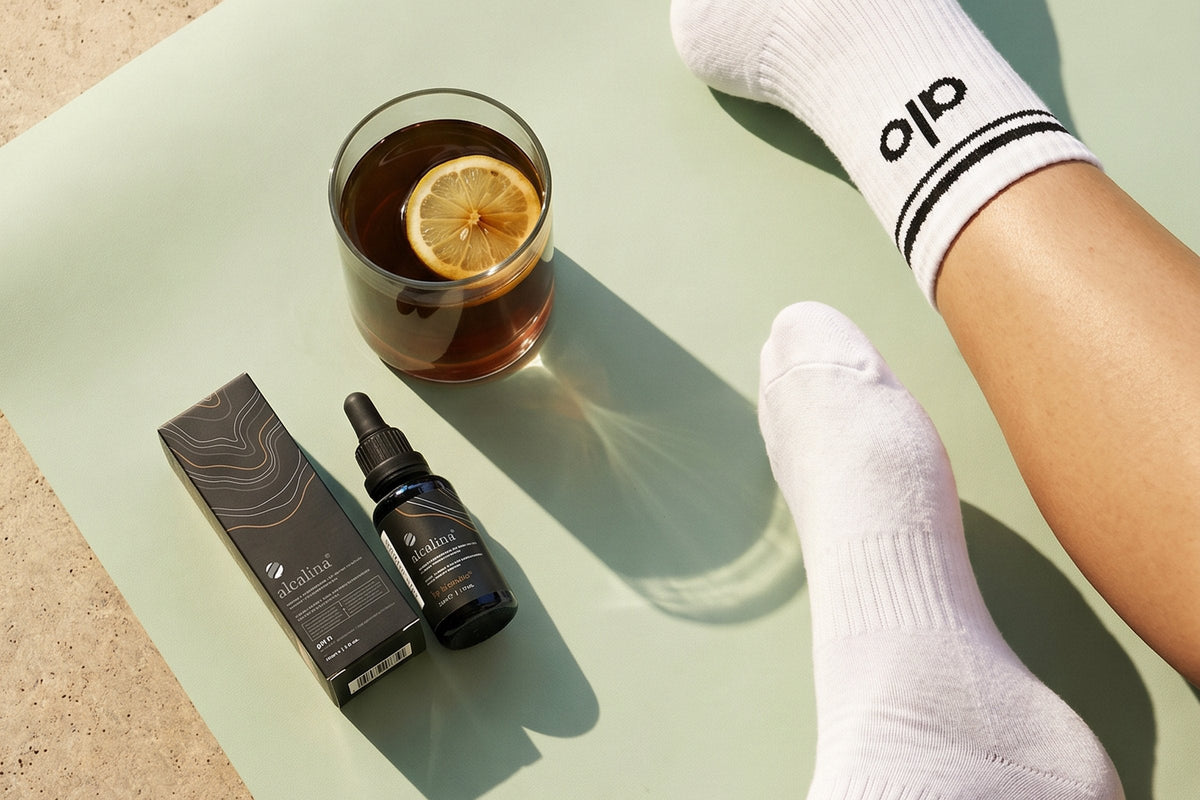 Un frasco cuentagotas de alcalina y un vaso junto a una esterilla de yoga