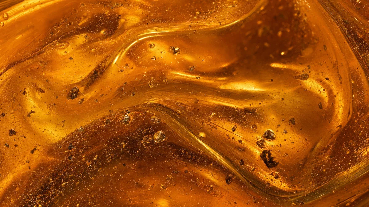 Concentrado mineral espeso de color ámbar dorado iluminado desde atrás, girando lentamente