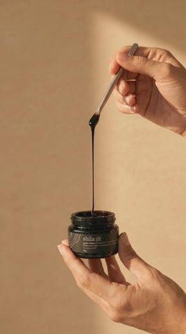 Un hilo largo de resina de shilajit dorado se eleva desde un tarro abierto.